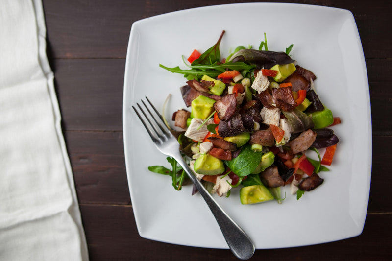 Colorful nutrient-rich salad with avocado, greens, and grilled meat on plate.